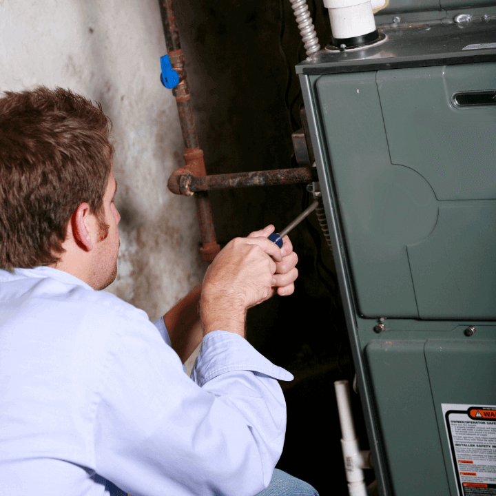 The image shows an HVAC specialist in a blue shirt conducting a furnace maintenance appointment.