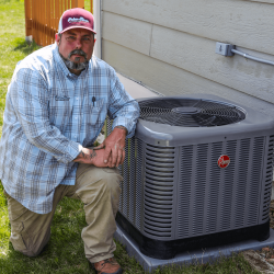 The image shows an HVAC expert kneeling on the ground and he's posing next to an outdoor HVAC unit.